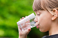 Child drinking water from a clear cup, highlighting the importance of fluoride in dental health and community water supplies.
