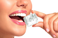 Woman holding ice cube near mouth, illustrating ice consumption and its potential effects on dental health.