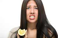 Woman grimacing while holding a lemon slice, illustrating the negative effects of lemon juice on teeth enamel.