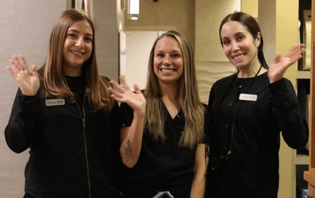 Dental hygiene team members smiling and waving, wearing black scrubs, in a welcoming dental office setting at Water Tower Dental Care.